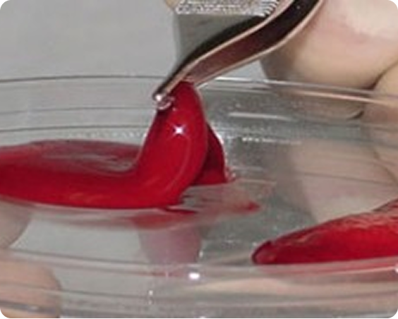 Red substance being lifted by tweezers from clear plastic container with two red blobs inside.