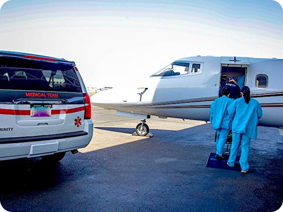 Medical team members in blue scrubs boarding a white medical jet near a medical SUV labeled Trinity.