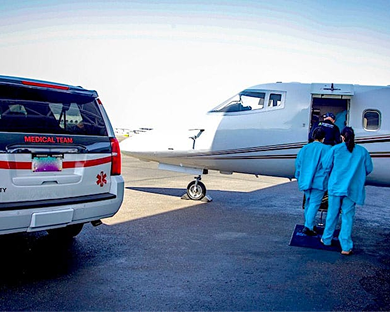 Medical team in blue scrubs boarding a small private jet next to a medical team SUV on an airstrip.