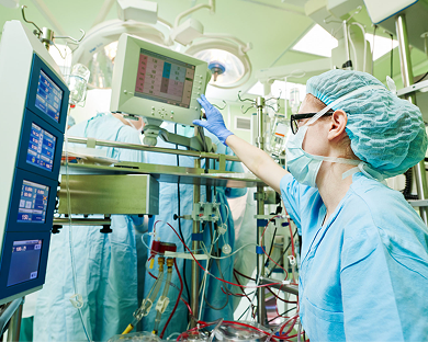 Medical professional adjusts monitor in operating room with surgical equipment and lights.
