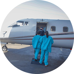 Medical team in blue scrubs boarding a private jet on an airfield.