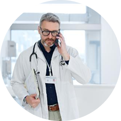 Middle-aged male doctor wearing glasses and white coat talking on phone while holding clipboard.