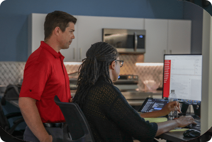 Group of nine people in red shirts standing in front of large monitors on a wall.