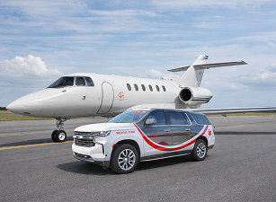 White private jet on runway with a white and red medical emergency SUV in front.