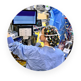 Medical professional in scrubs and EEG cap monitoring brain activity on screens in a clinical setting.