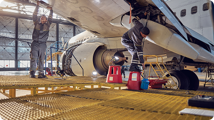 Aircraft technician in high-visibility jacket inspecting plane landing gear compartment with flashlight.