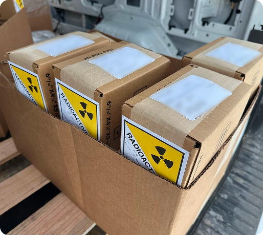 Cardboard box containing smaller boxes labeled with radioactive warning signs in a vehicle.