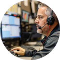 Man wearing headset and speaking while working on a computer in an office setting.
