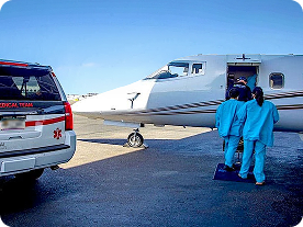 Medical team members in blue scrubs boarding a white medical jet near a medical SUV labeled Trinity.