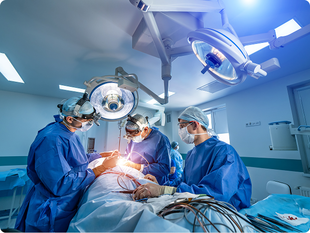 Three surgeons in blue scrubs performing surgery under bright operating room lights.