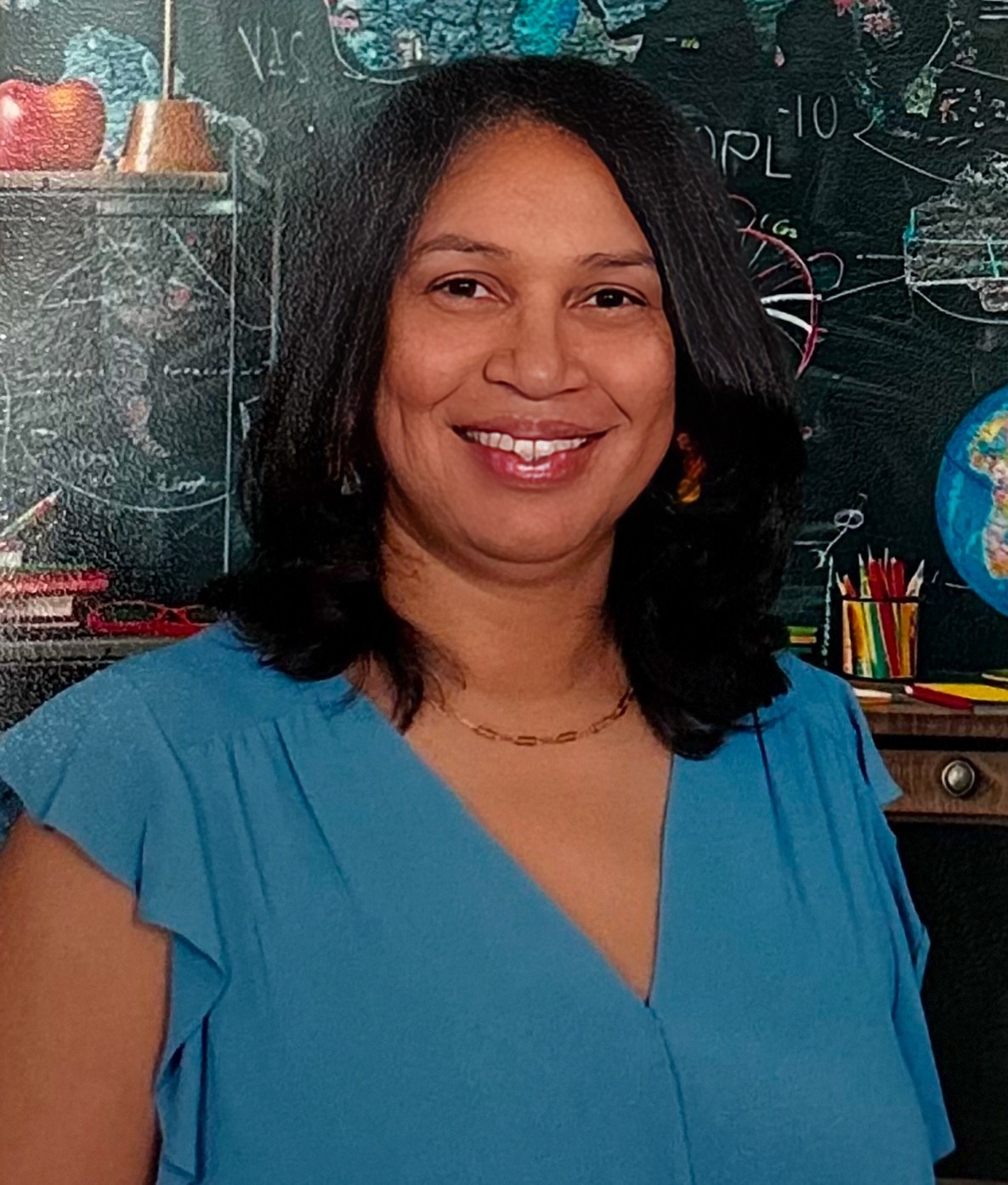 Staff member I. McNab smiling in front of a classroom chalkboard