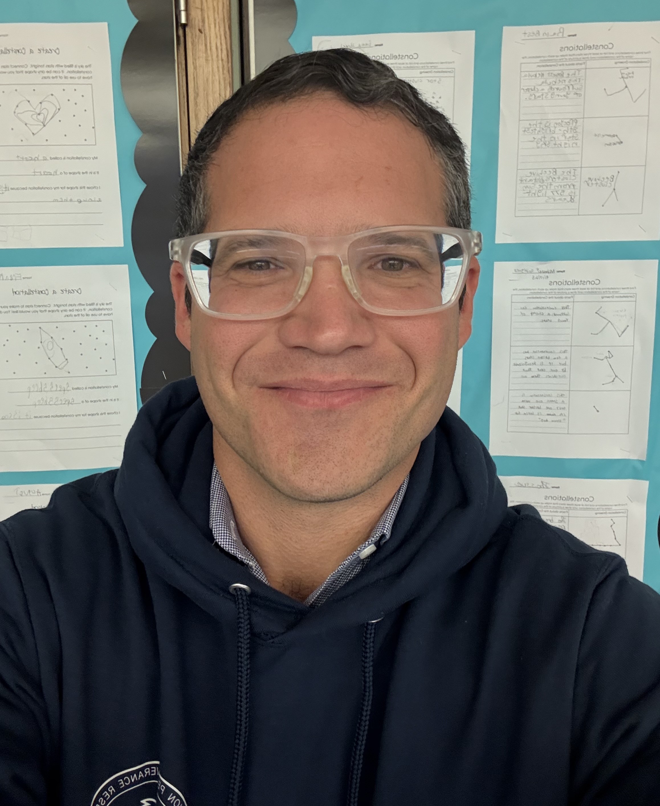 Teacher E. Leibowitz smiling in front of student constellation work