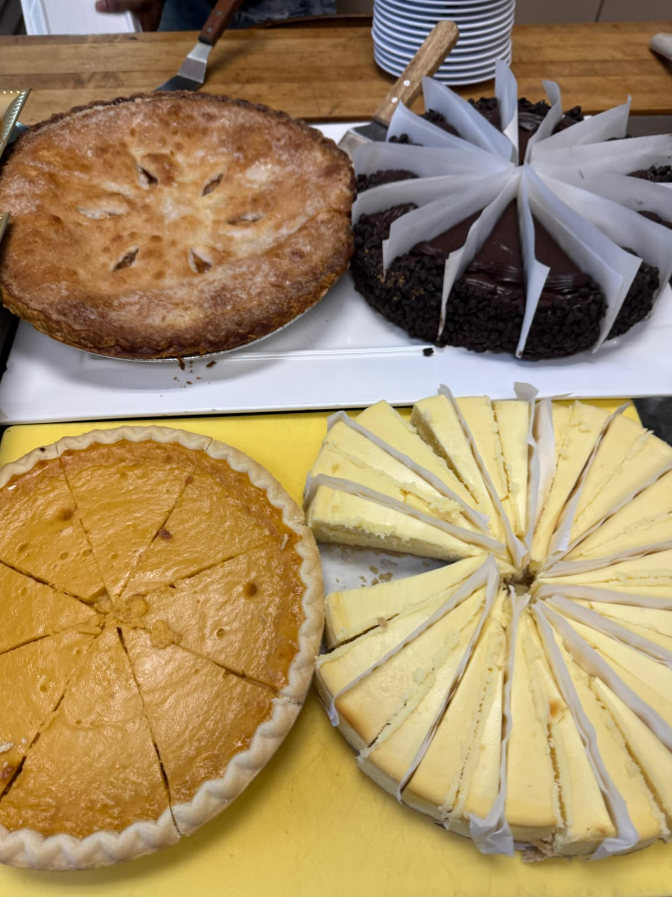Four desserts: a whole apple pie, a chocolate cake sliced with parchment paper between pieces, a pumpkin pie sliced into wedges, and a cheesecake sliced with parchment paper between pieces.