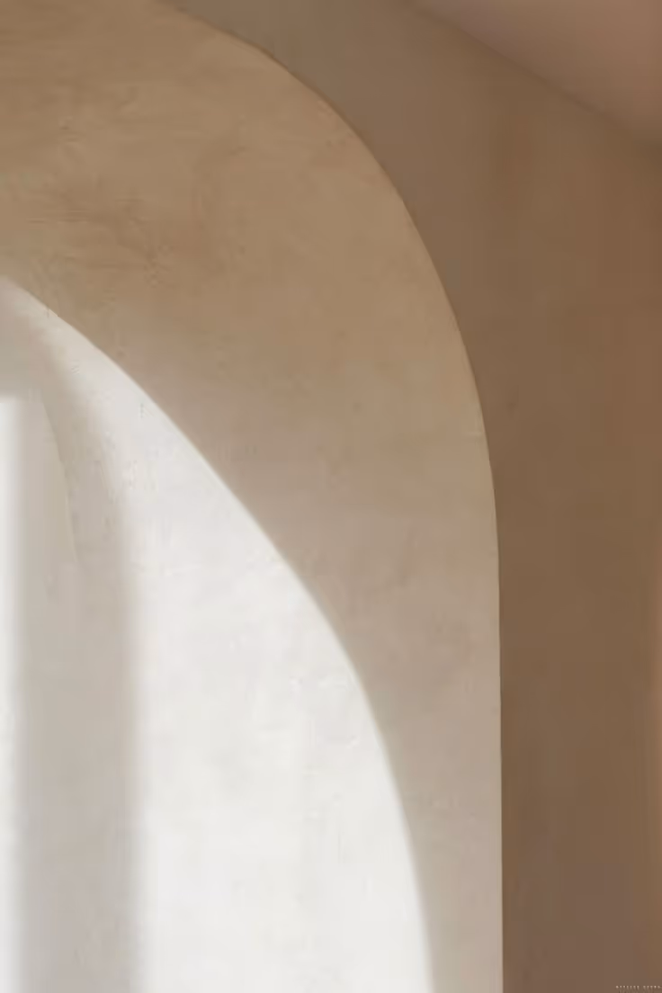 Soft natural light casting curved shadows on a beige arched wall.