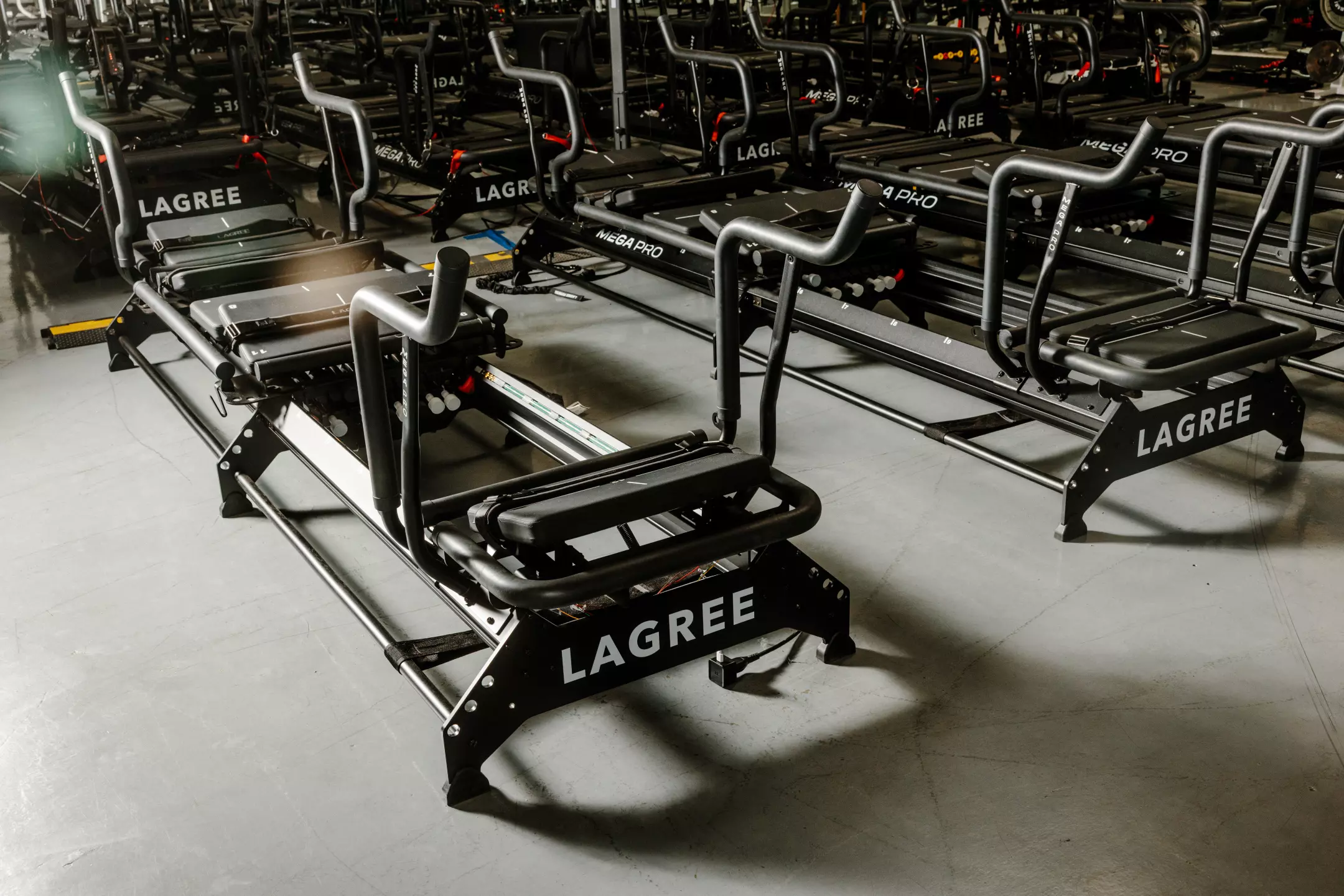 Rows of black Lagree fitness reformer machines lined up on a gym floor.