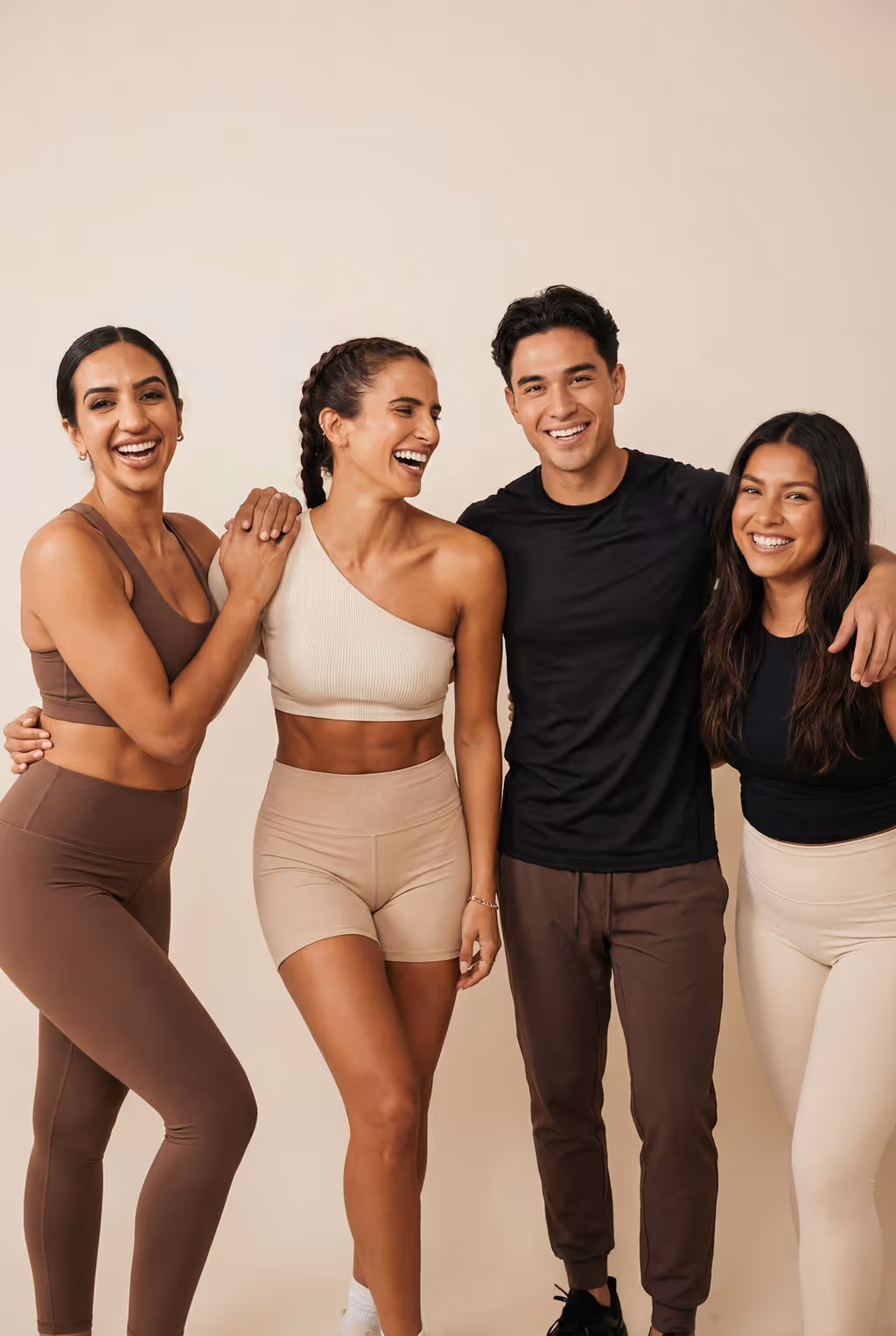 Group of four diverse young adults in activewear smiling and standing closely together against a plain background.