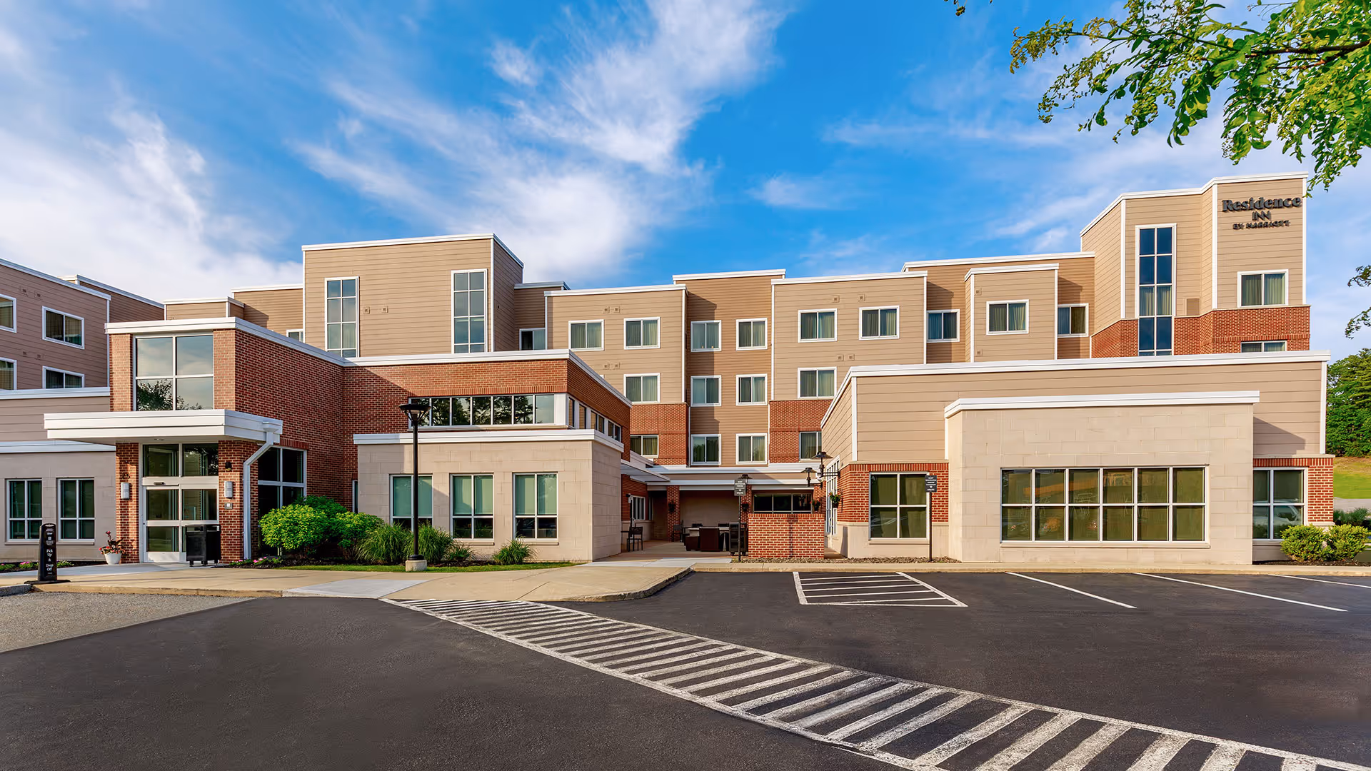 Modern four-story Residence Inn by Marriott building with beige and brick exterior under a partly cloudy blue sky.