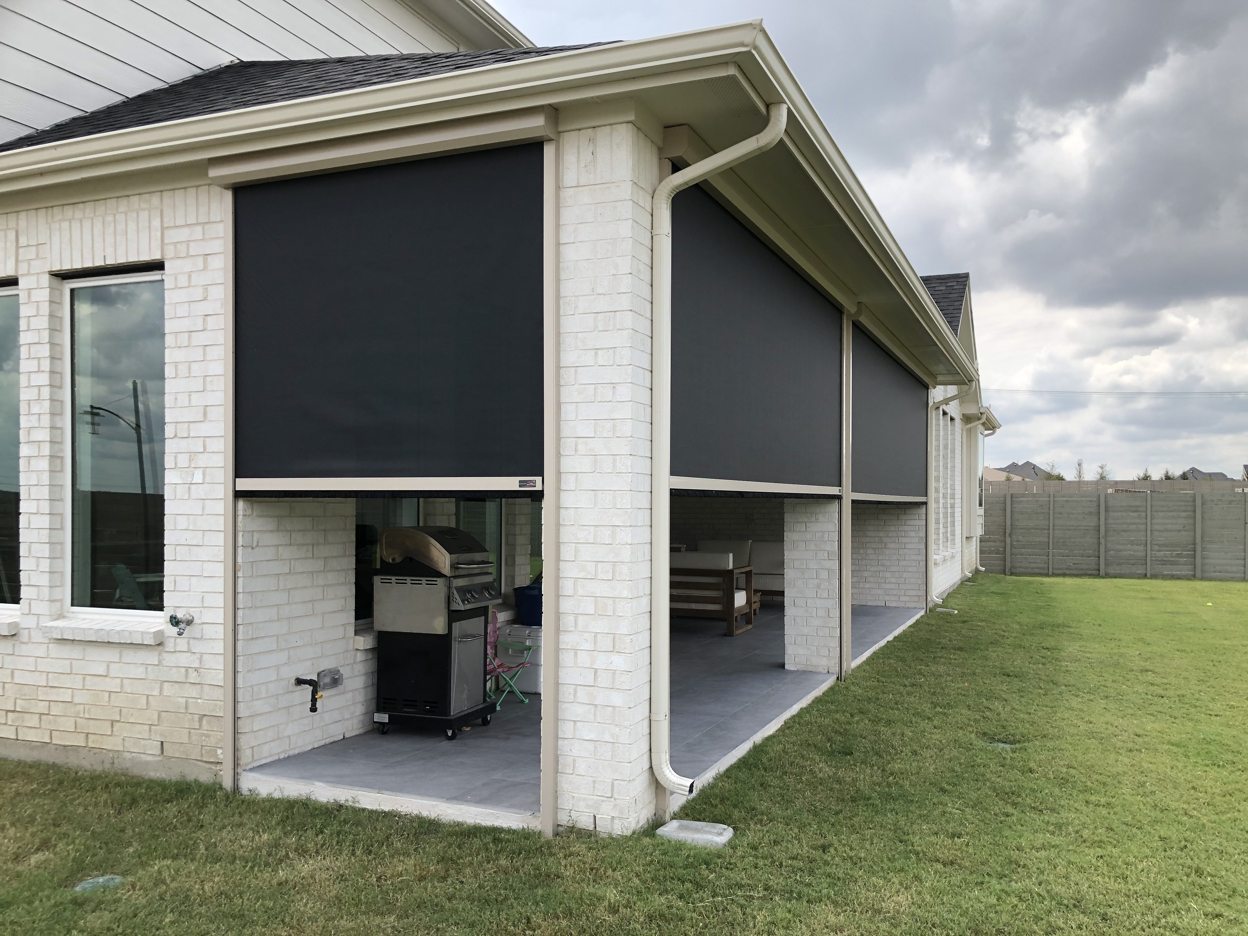 Outdoor patio area with black rolling security screens, brick house, grassy yard.