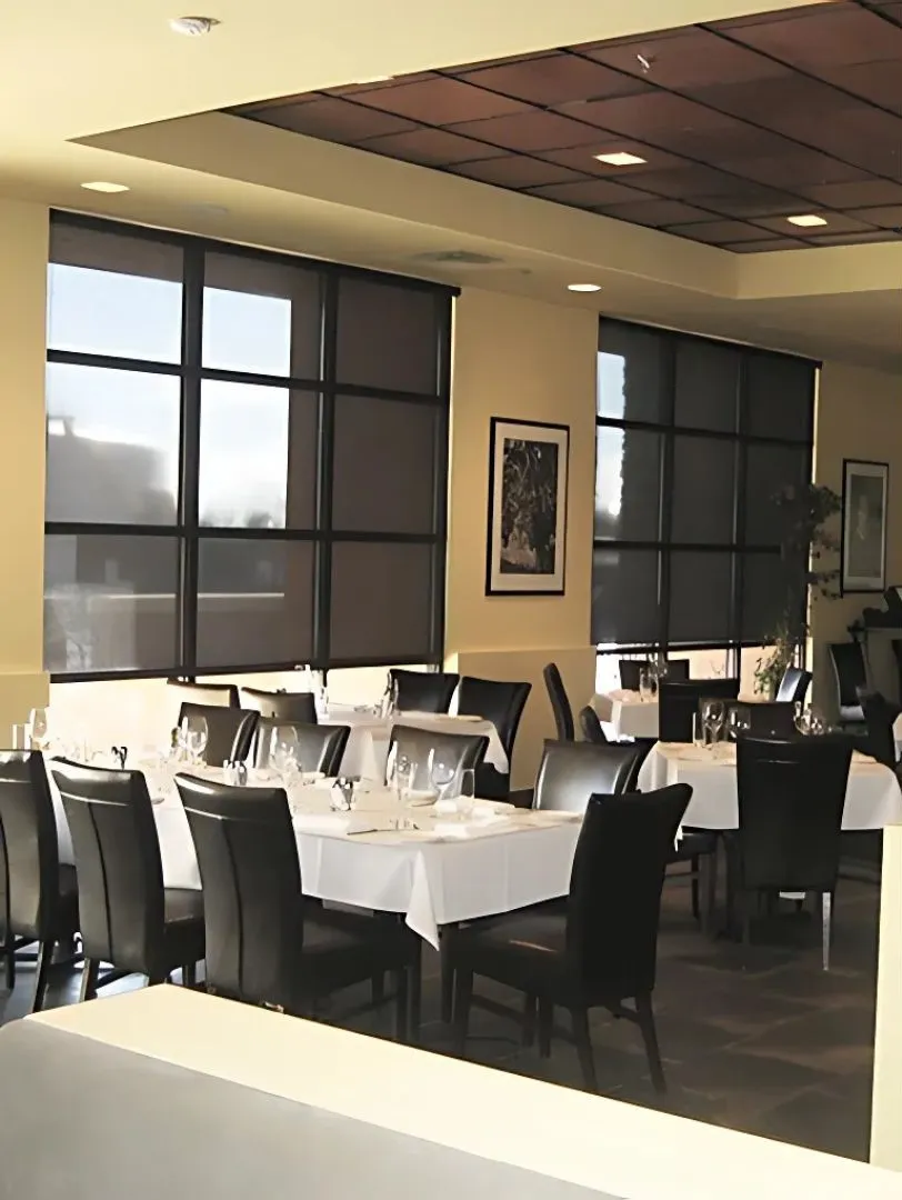 Elegant restaurant dining area with tables set with white tablecloths, glassware, and black leather chairs under soft lighting.
