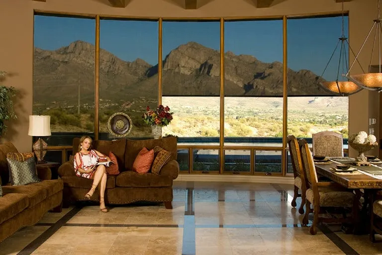 Woman sitting on a brown sofa reading a book in a living room with large windows showing a mountain view.