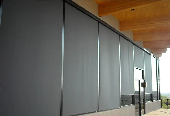 Exterior of a modern commercial building with large gray roll-down shades covering tall windows and a glass door under a wooden overhang.