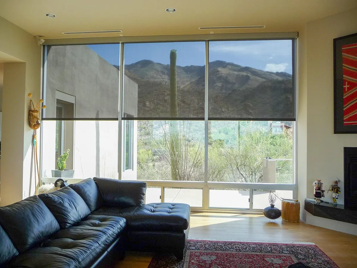 Living room with a black leather sectional sofa facing large windows with half-lowered gray roller shades and a mountain view.