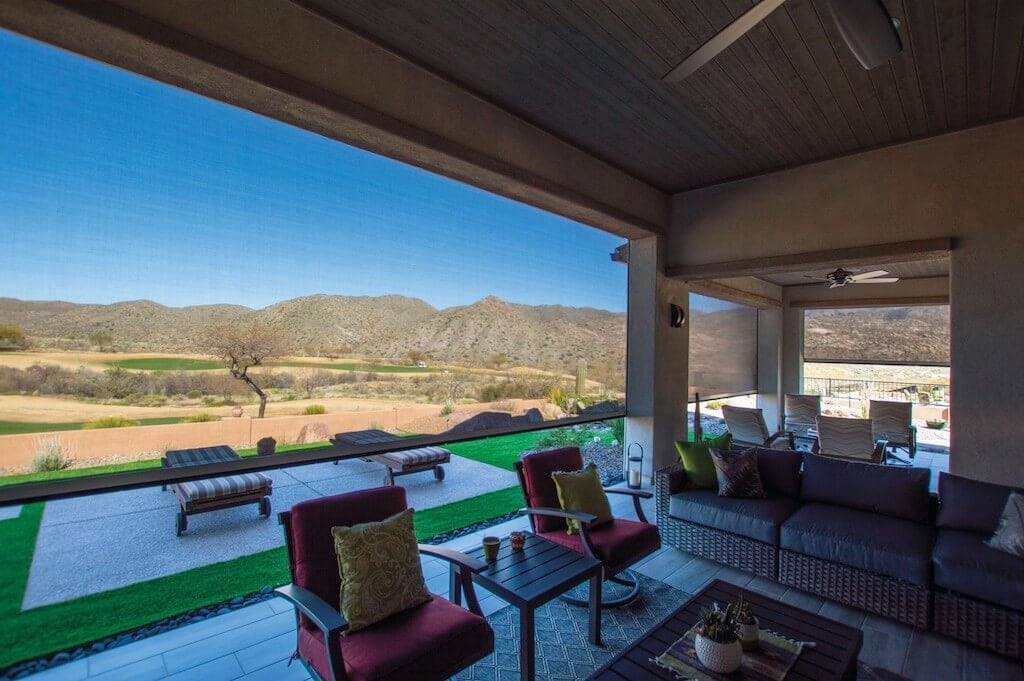 Covered patio with outdoor seating including red cushioned chairs and a wicker sofa, overlooking a scenic mountain and desert landscape.