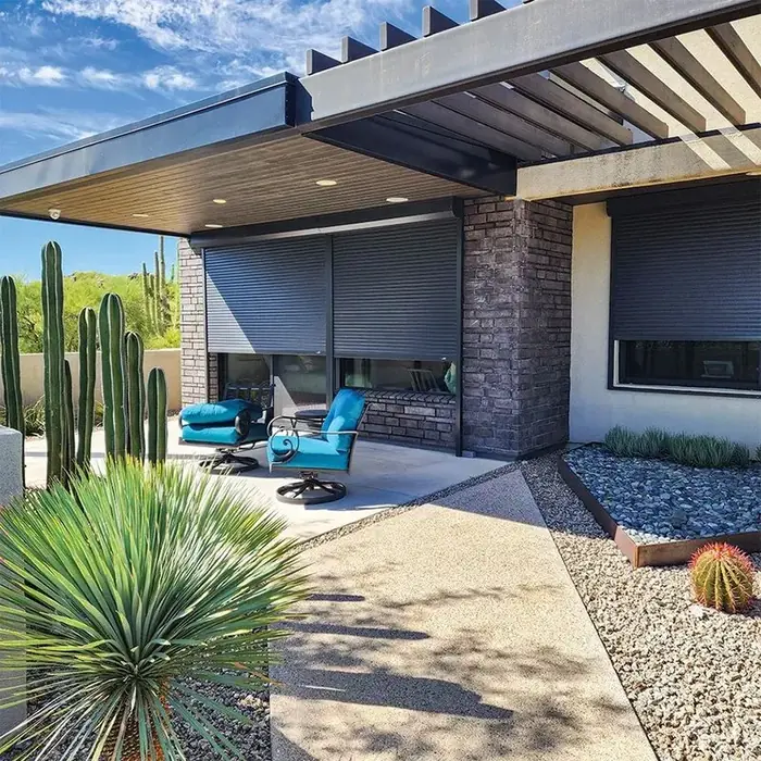 Modern patio with dark brick and metal accents, featuring blue-cushioned outdoor seating, desert landscaping with cacti and gravel mulch, and a sleek pergola.