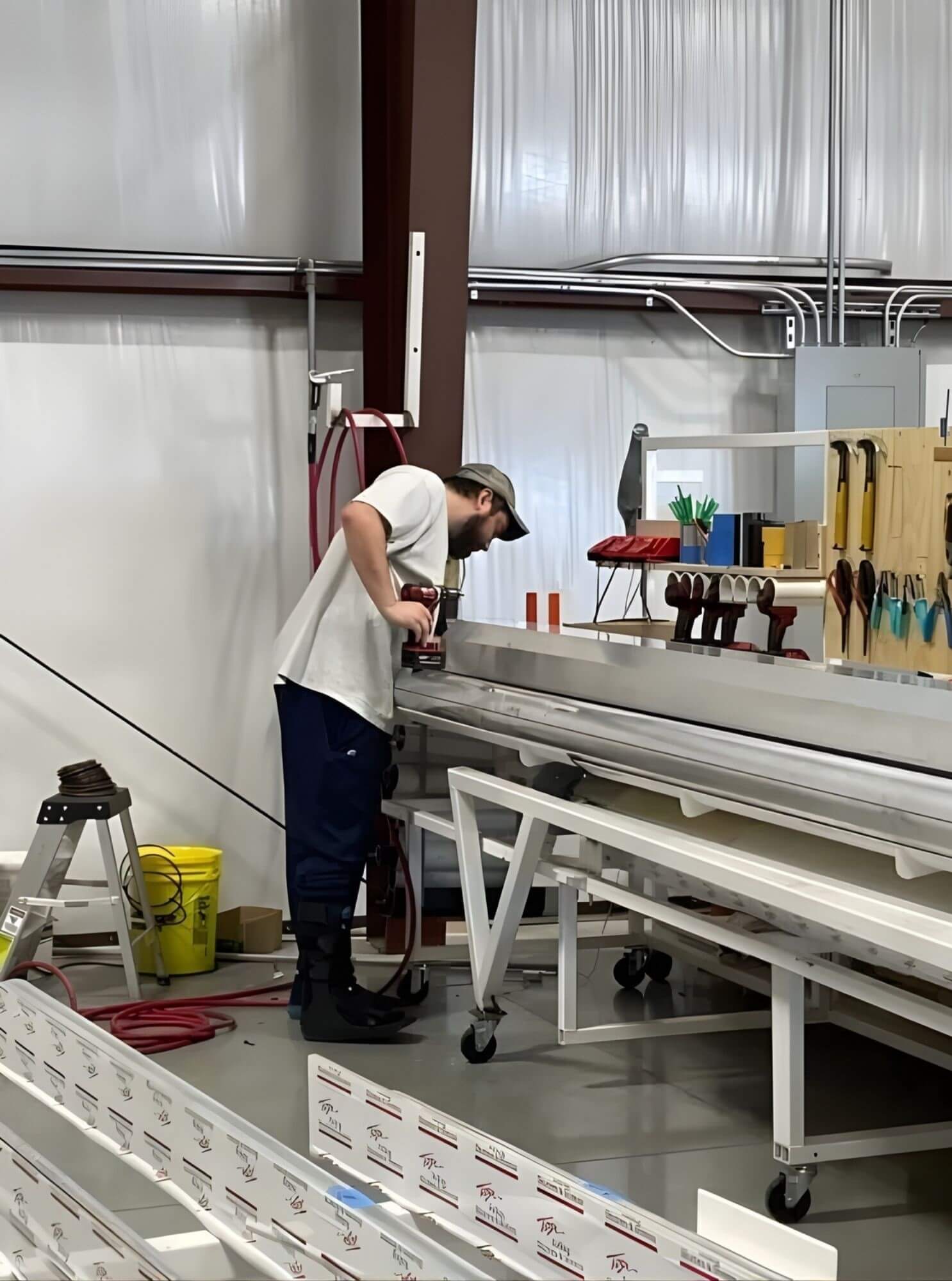 A worker in a factory setting operates machinery, assembling or inspecting components for rolling shutters; tools and materials are organized nearby, indicating a manufacturing process at Tucson Rolling Shutters.