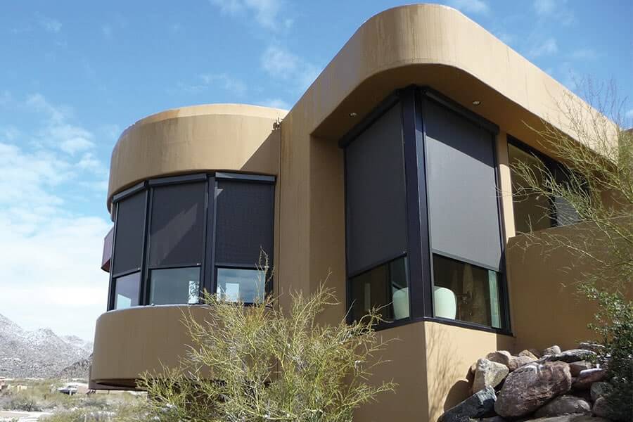 Modern desert home with curved architecture and large windows, surrounded by rocky landscape and clear sky.