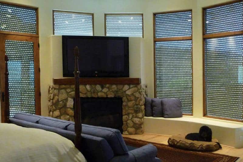 Room with stone fireplace, TV, and rolling shutters on windows.
