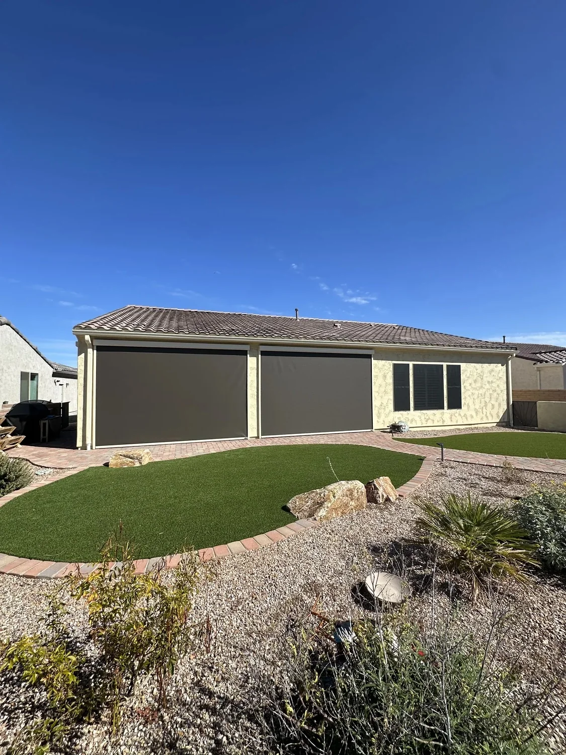 Two large brown solar screens on back of home with artificial turf and desert backyard