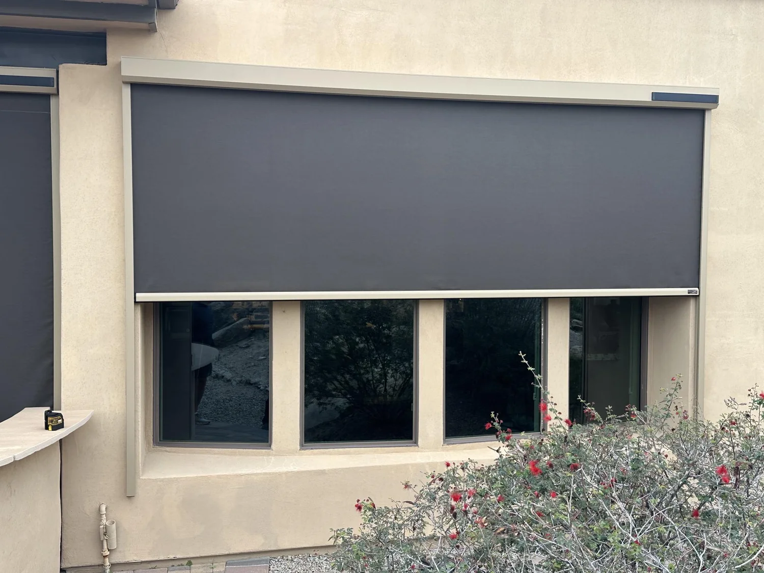 Charcoal solar screen installed over wide exterior window bank on stucco home