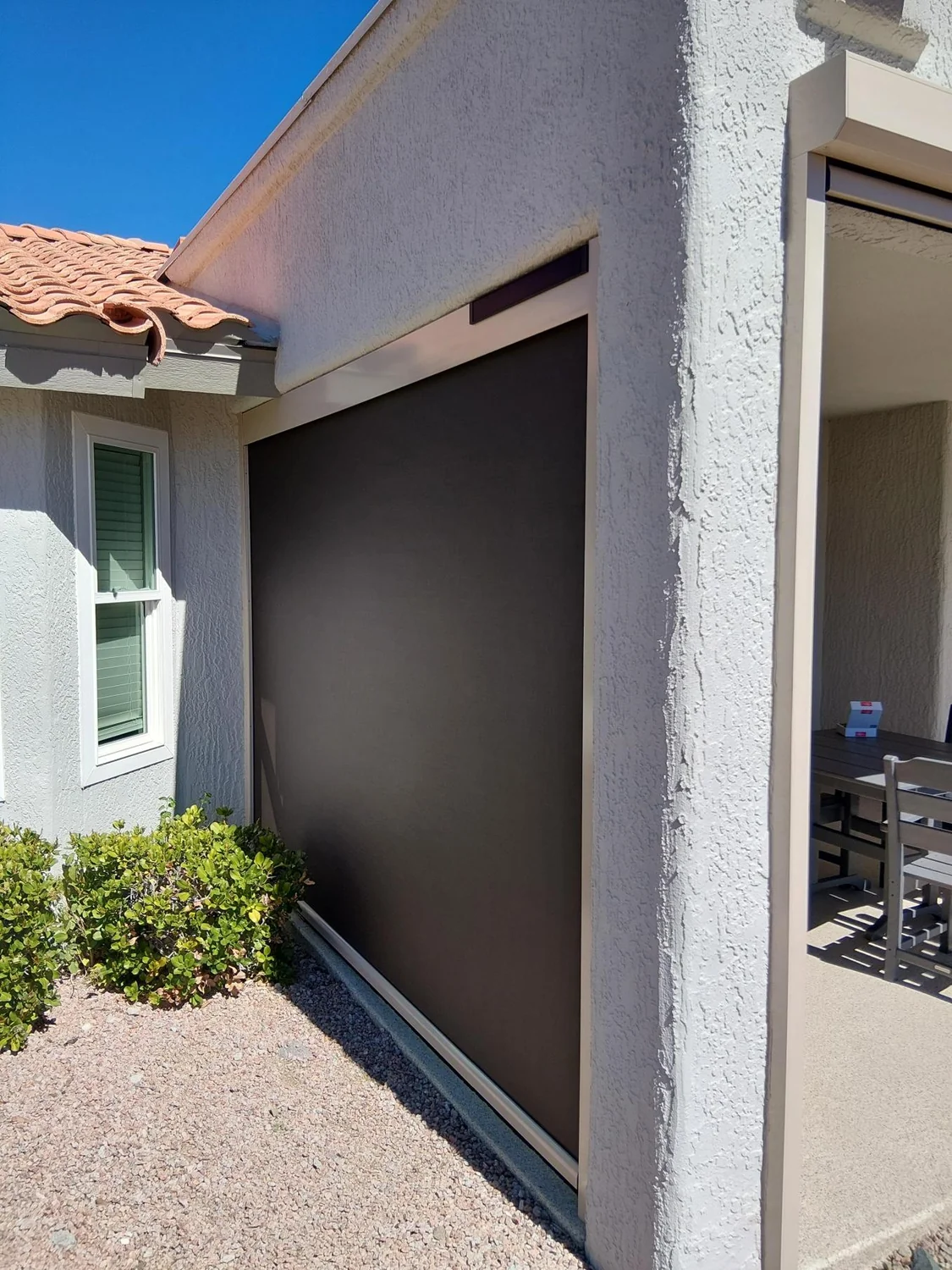 Single brown solar screen on side wall of white stucco home with tile roof and green landscaping