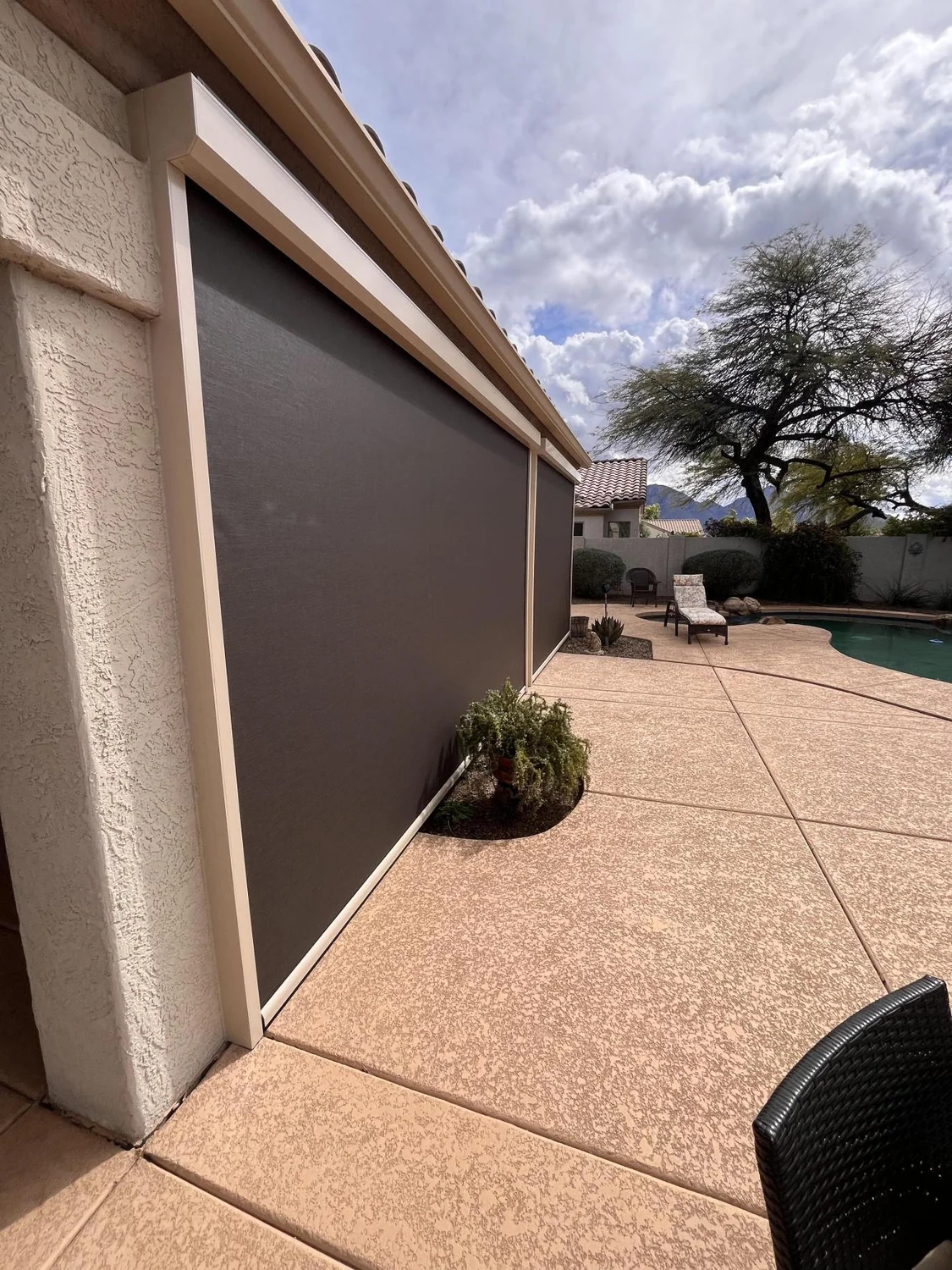Brown solar screen installed on stucco home exterior with swimming pool and patio in backyard