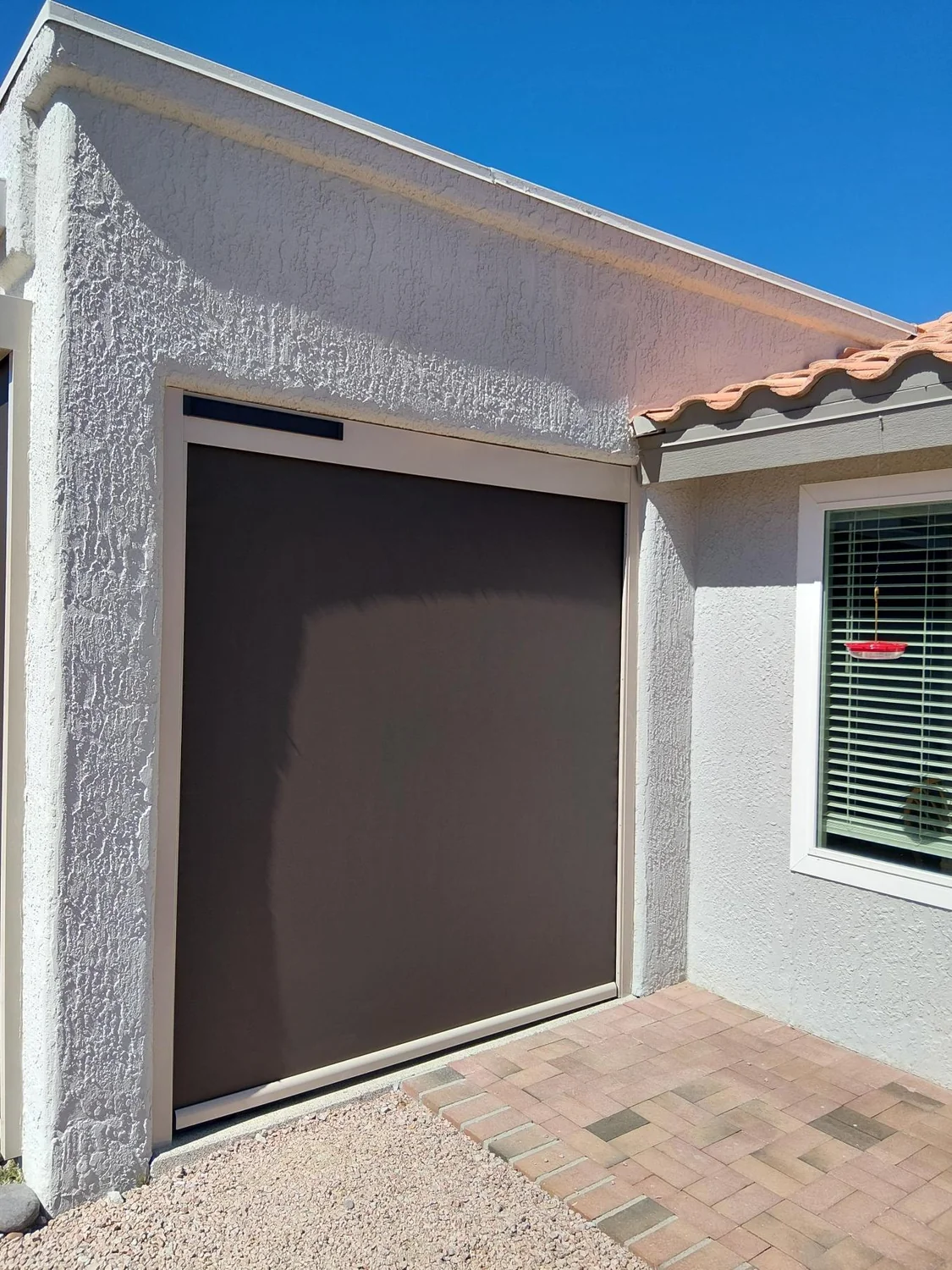 Single brown solar screen installed over window on white stucco home exterior