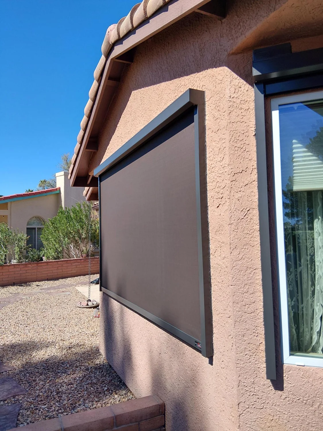 Brown solar screen on window of terra cotta stucco home with desert landscaping