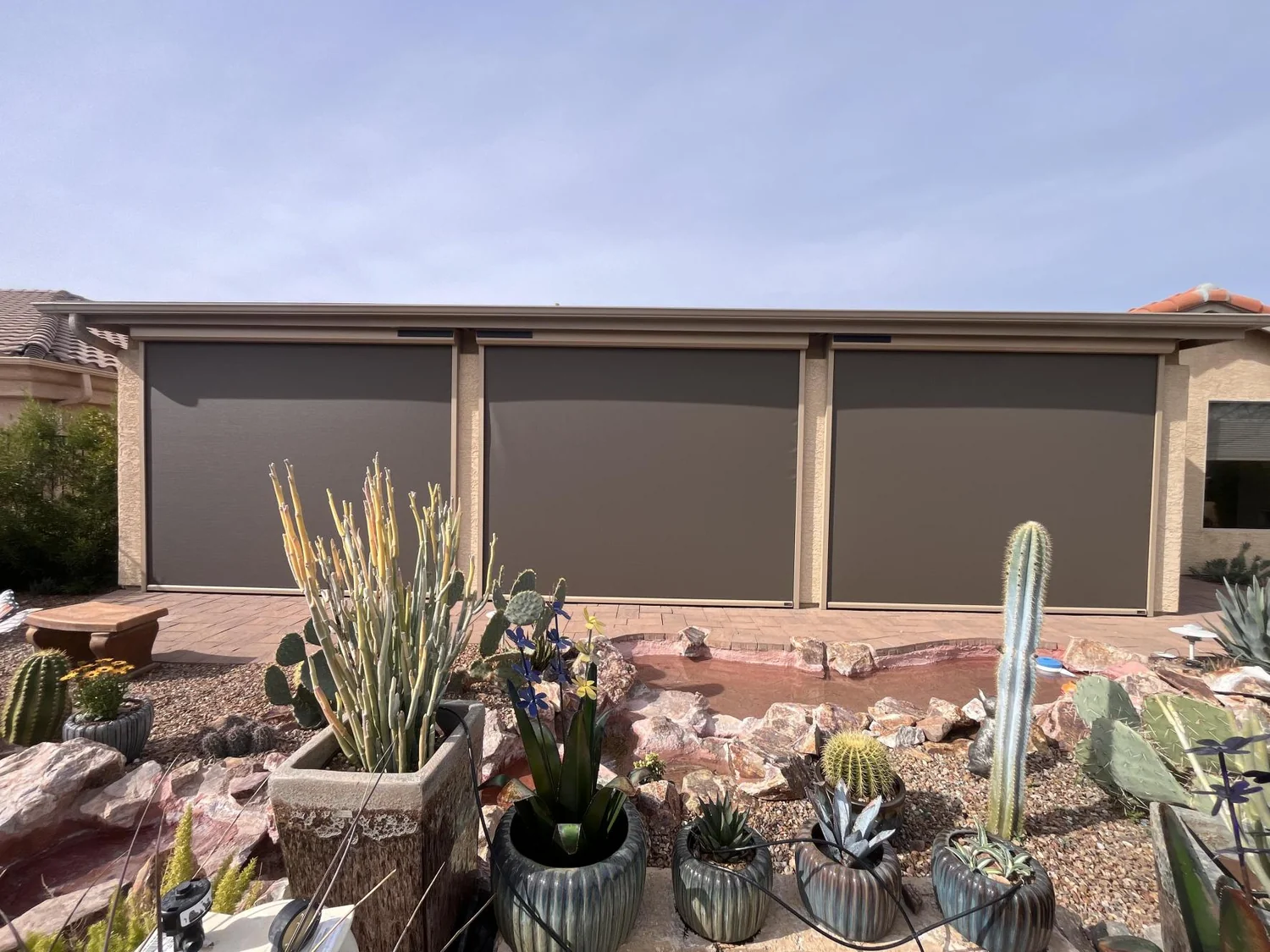 Three brown solar screens on back patio with cactus garden and water feature in backyard
