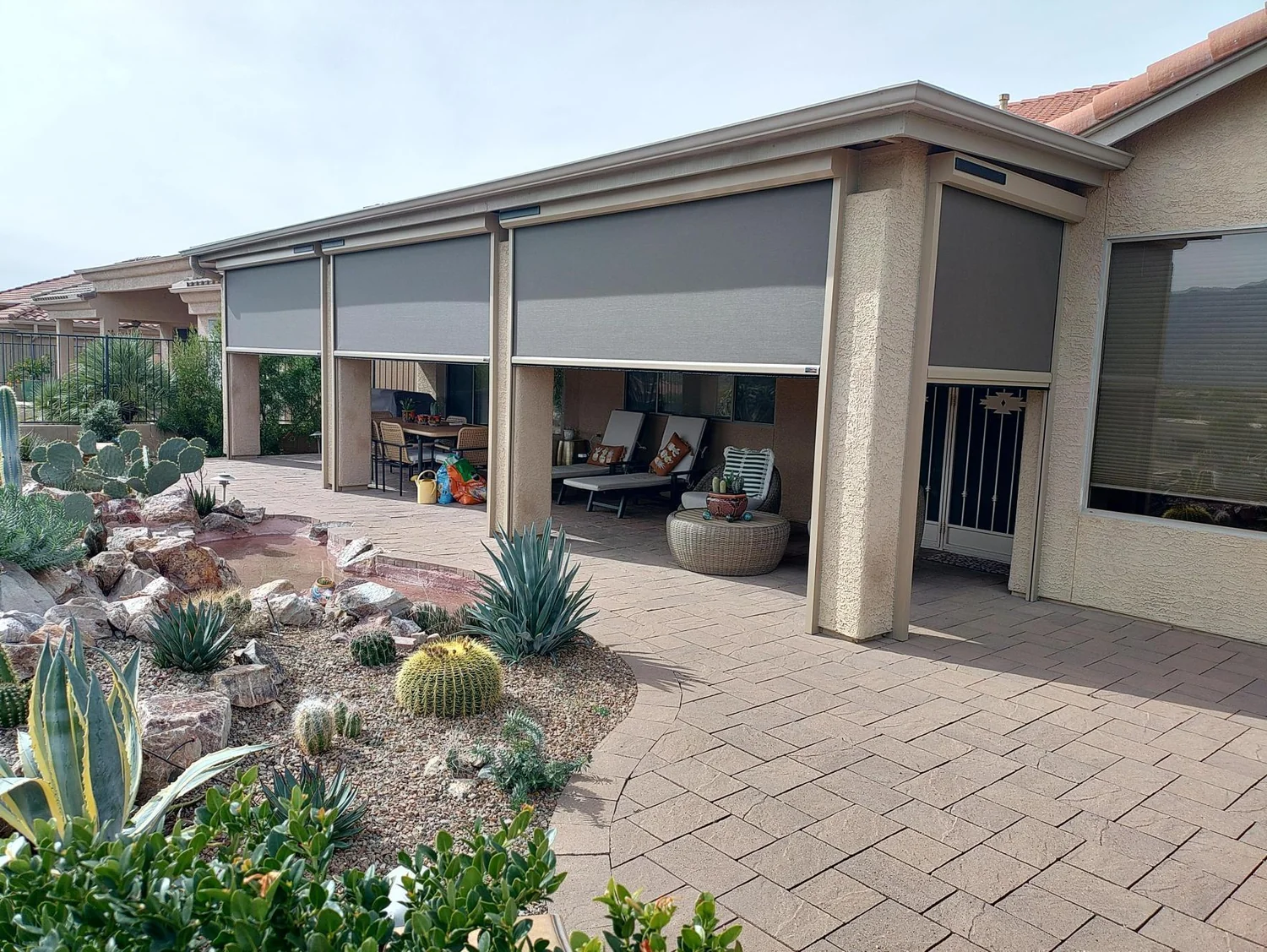 Solar screens partially raised enclosing patio with desert cactus garden in foreground