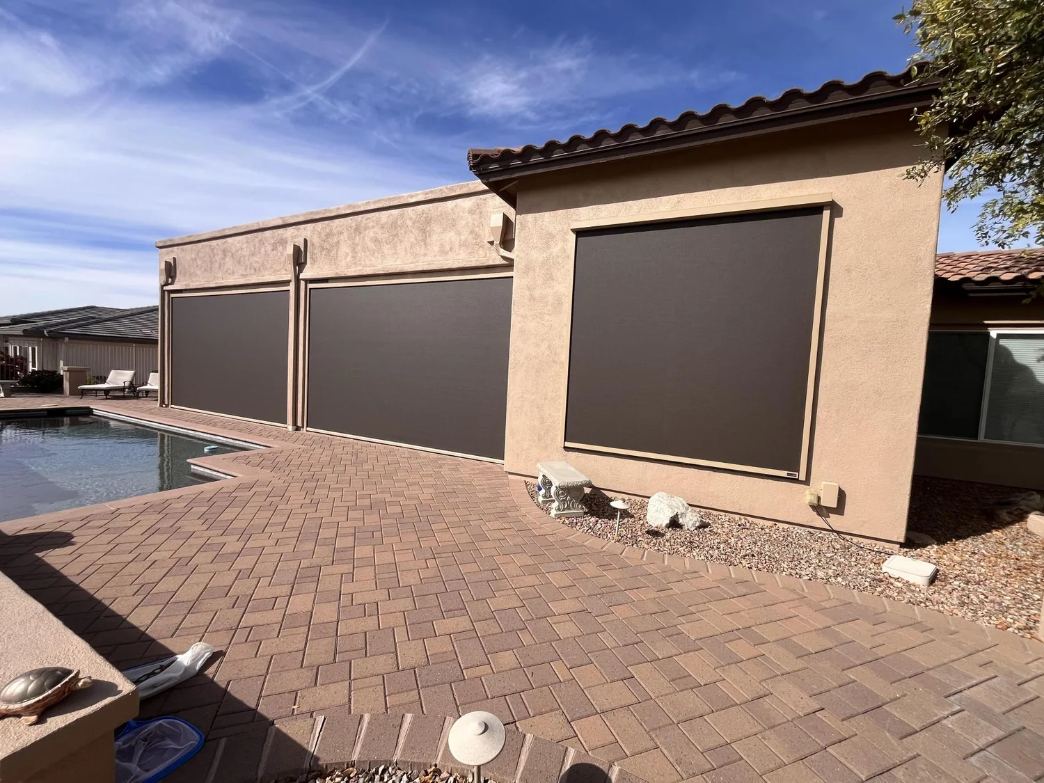 Three brown solar screen panels on back of beige home with backyard swimming pool
