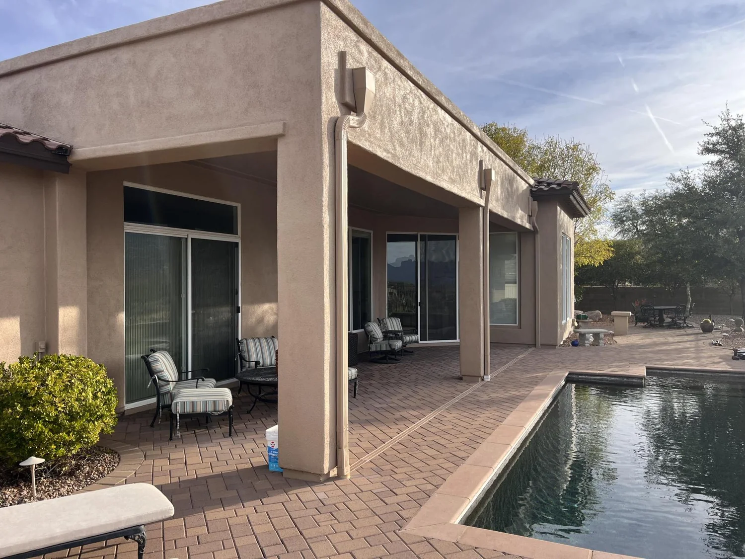 Solar screens installed on pool patio of stucco home with outdoor lounge chairs