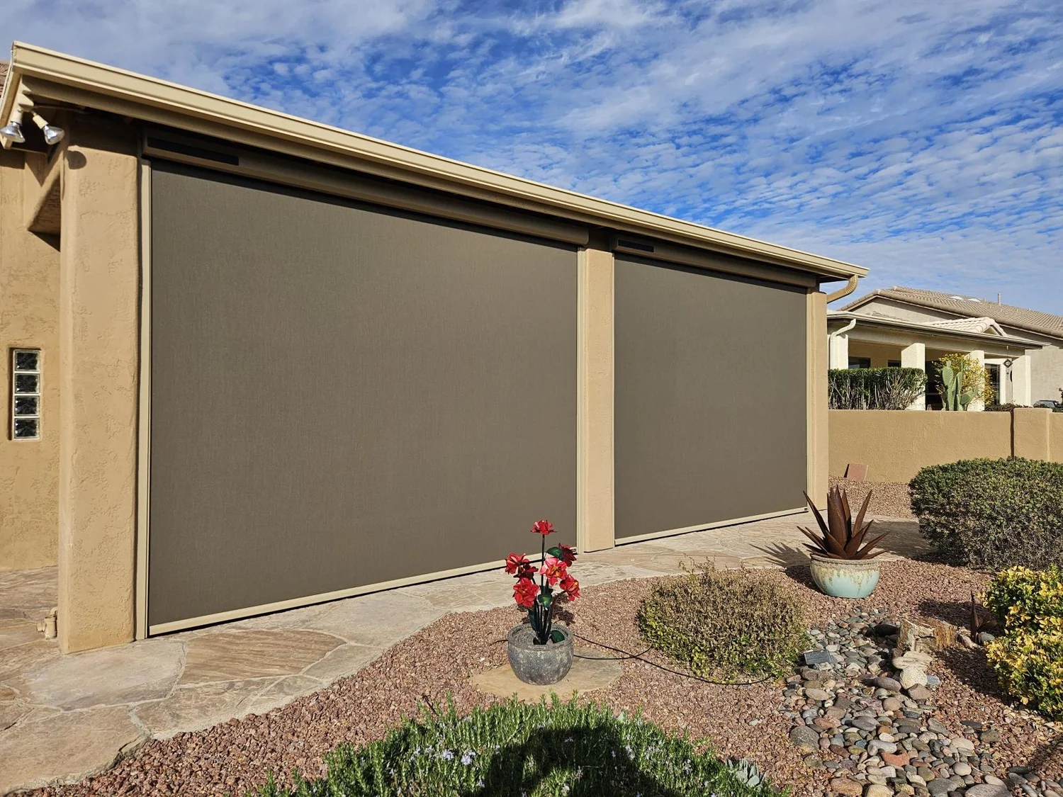 Two large brown solar screens on side wall of beige home with desert plants and blue sky