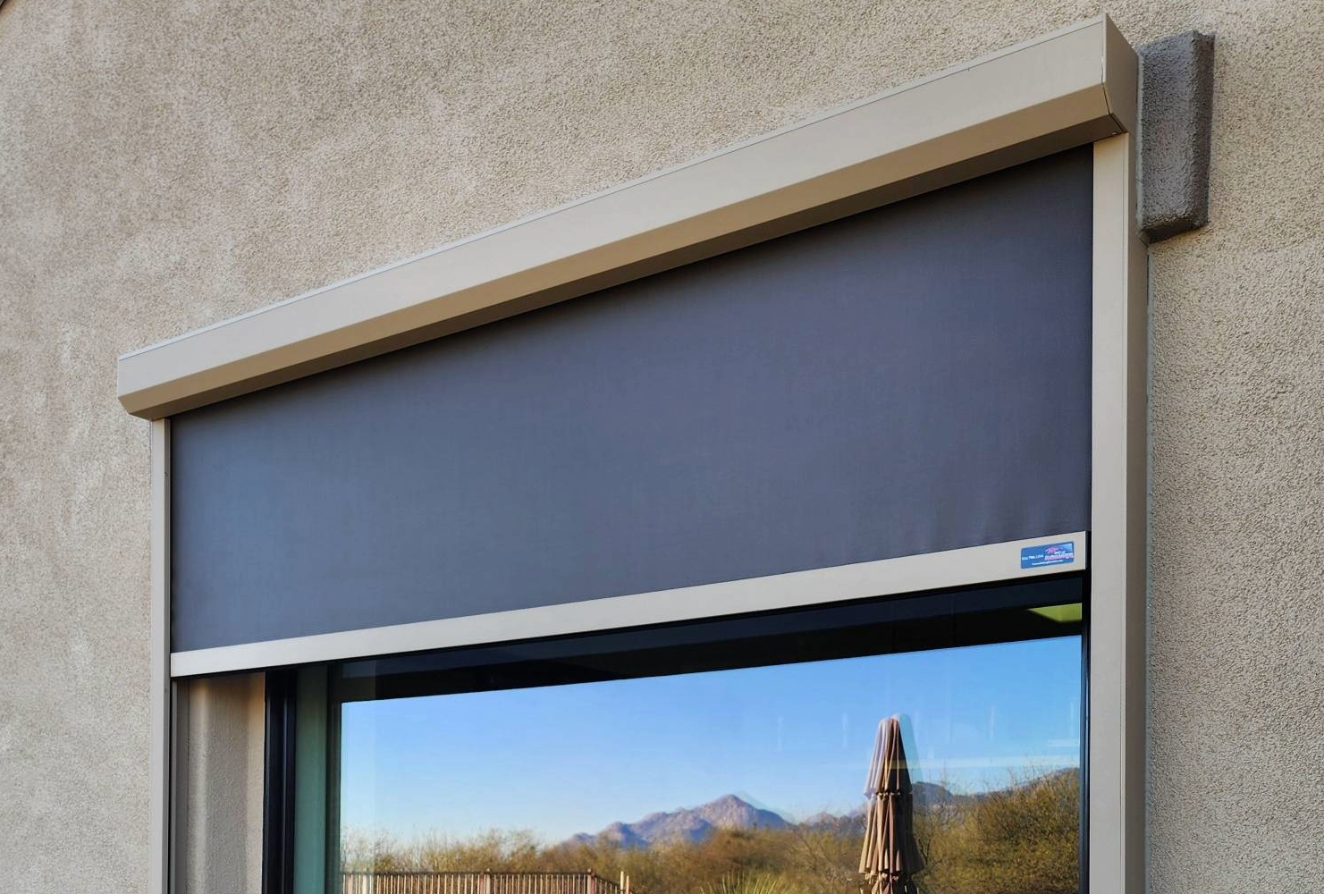 Black solar screen partially covering a sparkling home window. The mountains and shrubbery are reflected on the glass.