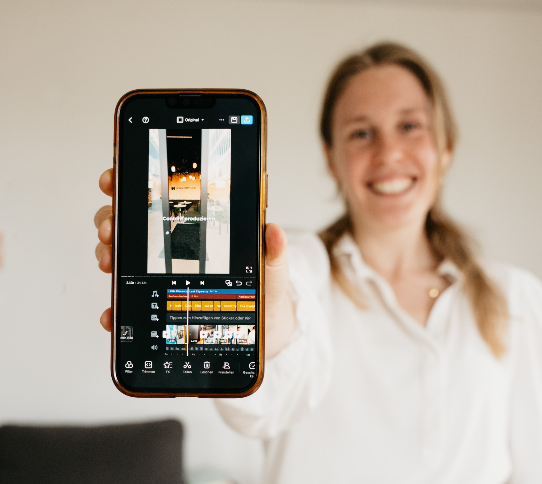 Smiling woman in white shirt holding a smartphone showing a video editing app with timeline and controls.