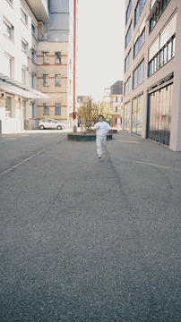 Man in white clothes running joyfully on an urban street between modern buildings in bright daylight.