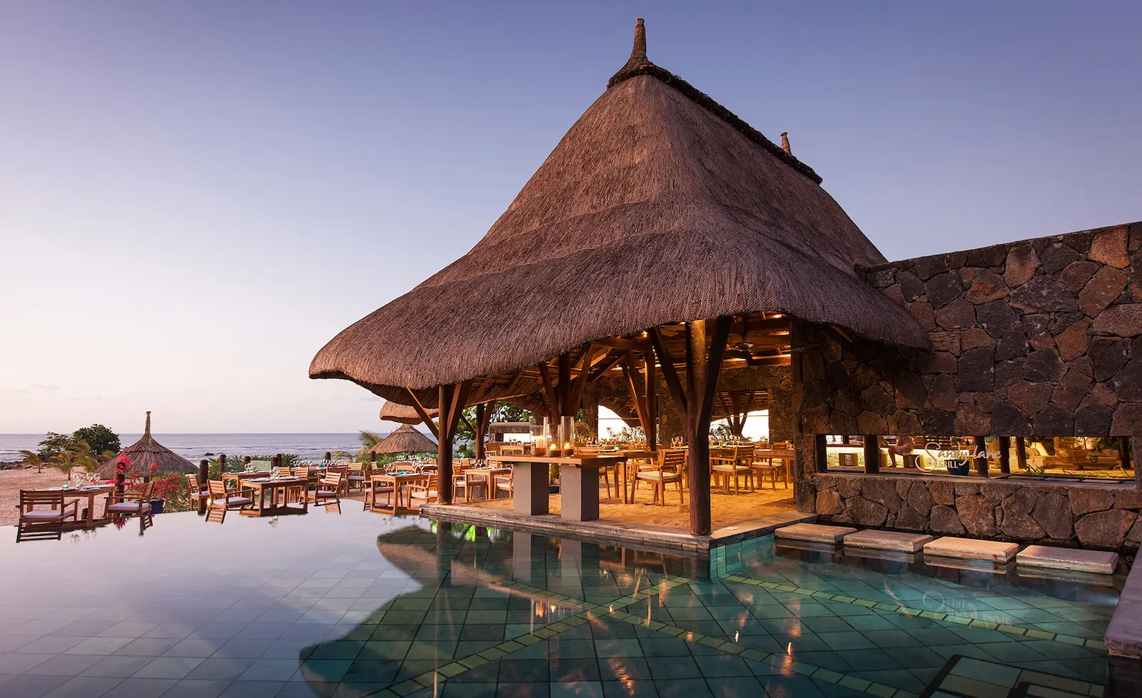 Open-air dining pavilion with thatched roof beside a pool and ocean view in Mauritius—Island Lilly’s tranquil setting for relaxed meals and coastal indulgence