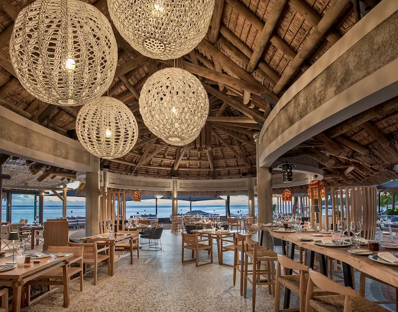 Elegant indoor dining area with woven light fixtures, wooden furniture, and ocean views—Island Lilly’s coastal culinary experience ideal for honeymoon and family