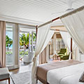 Elegant tropical-style bedroom with soft linens, warm wood accents, and natural light filtering through lush greenery, inviting rest and renewal.