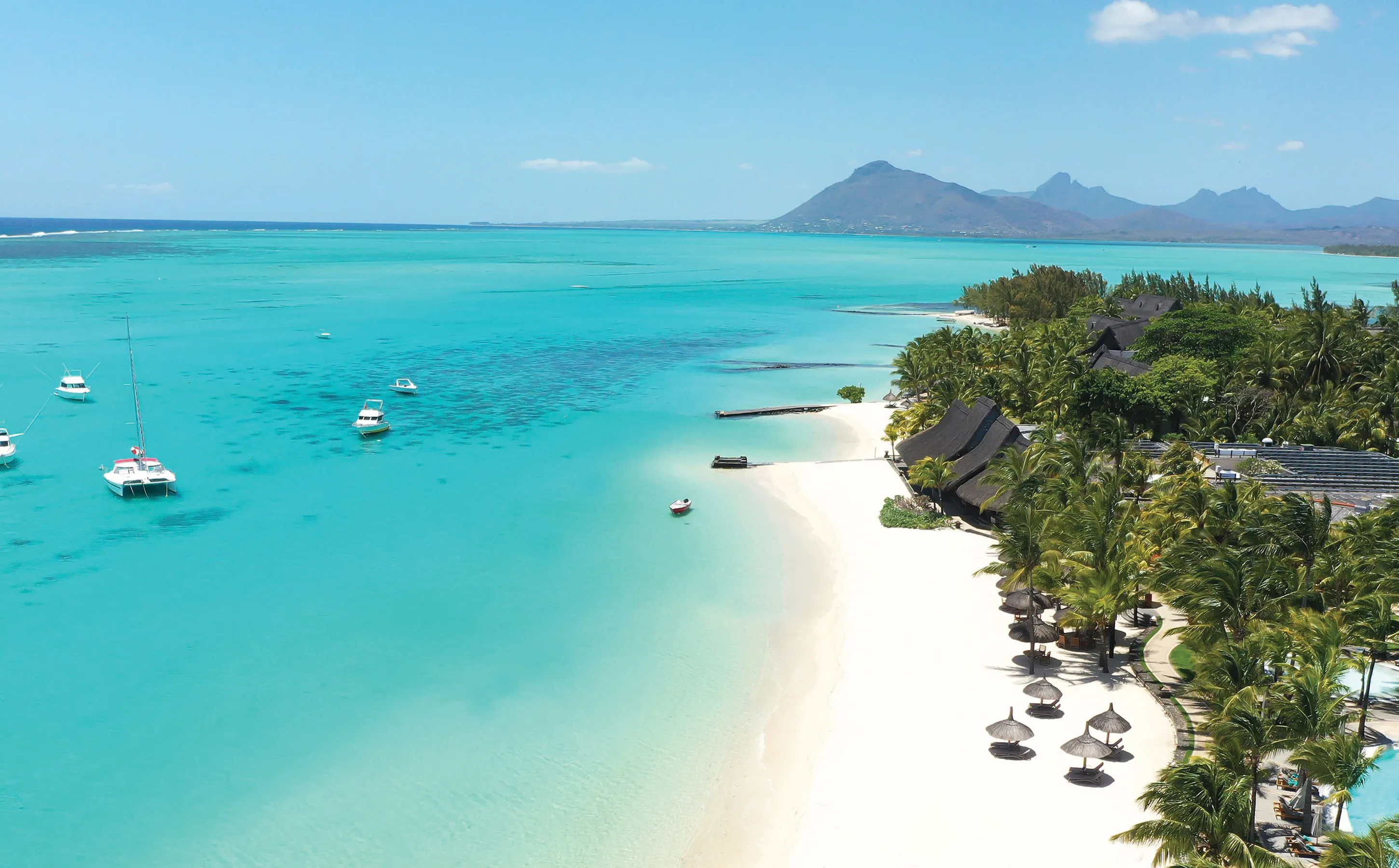 Tropical lagoon in Mauritius with anchored boats, palm-fringed beach, and mountain backdrop—Island Lilly’s signature blend of serenity, culture, and barefoot luxury