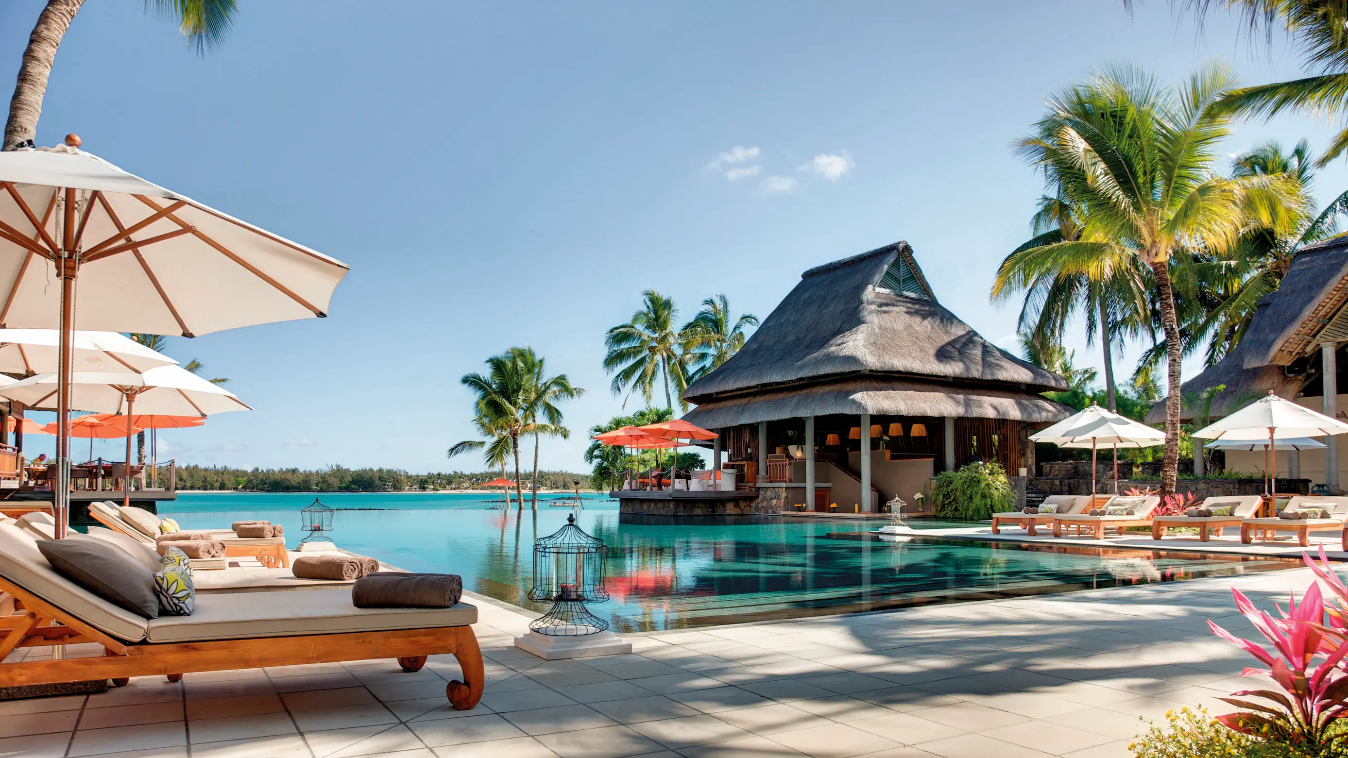 Tropical resort in Mauritius with palm trees, thatched-roof villas, poolside loungers and ocean views.